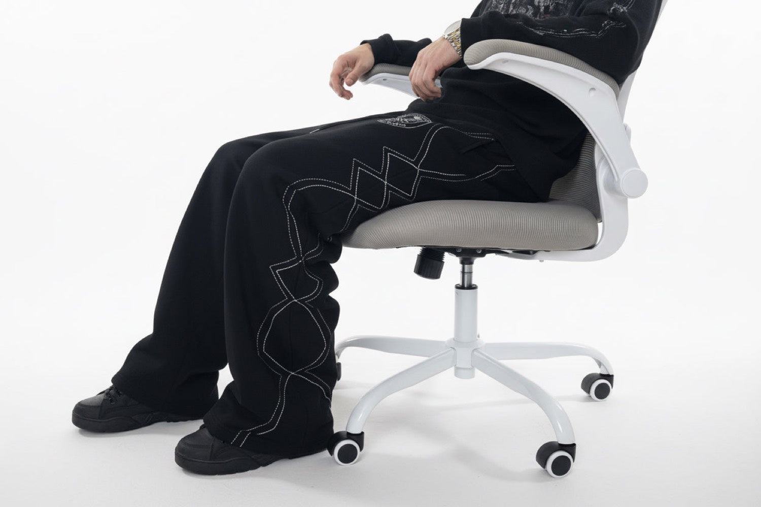 The Royal Logo Sweats worn seated, white contrast stitching tracing the outseam from hip to hem.