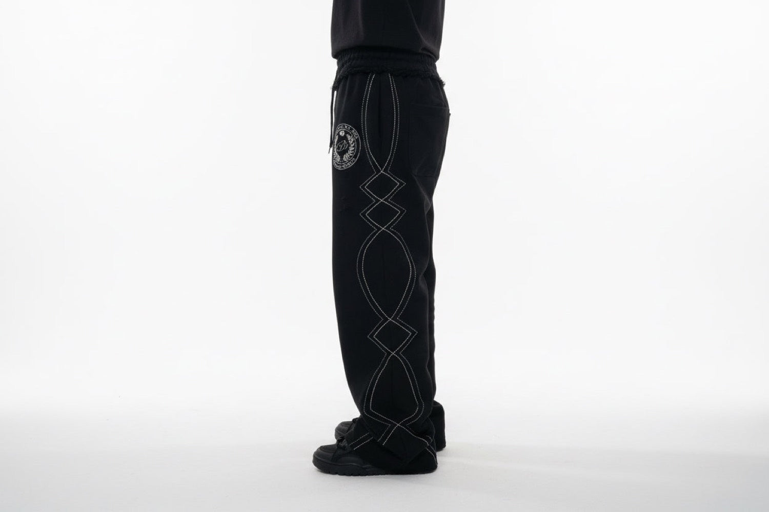 The same sweats worn, side view, showing the wide-leg drape and the embroidered crest at the hip.